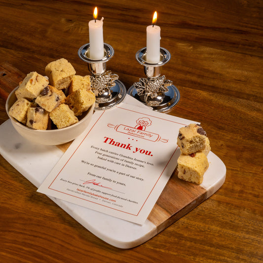 Lit candles beside a bowl of mandel bread and a Lazar Family Bakehouse thank-you card, set for a holiday dinner